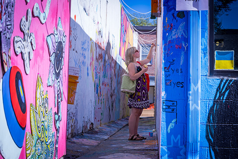 A woman stands in an alleyway covered in brightly painted murals.