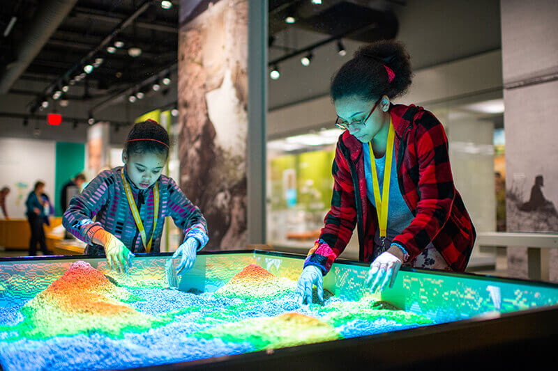 Two people moving sand in an interactive museum video display.