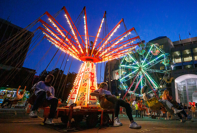 A ride covered in blinking lights spins riders around at a carnival at night.