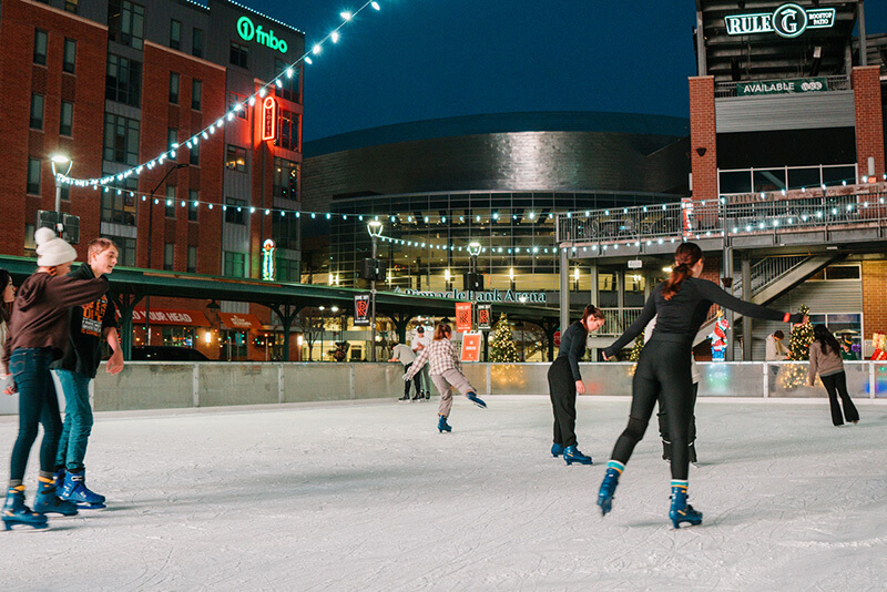 Ice skaters enjoy gliding across a rink at night under strings of lights.