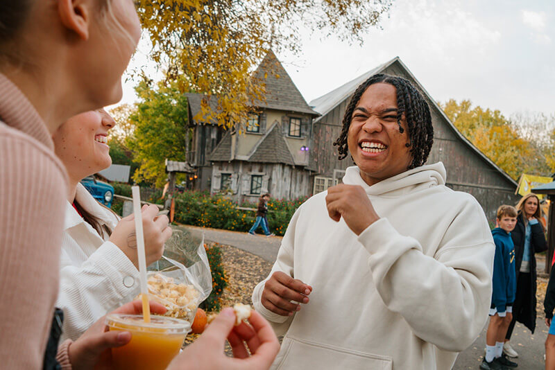 A man laughs with female friends with haunted houses in the background at Rocca Berry Farms.