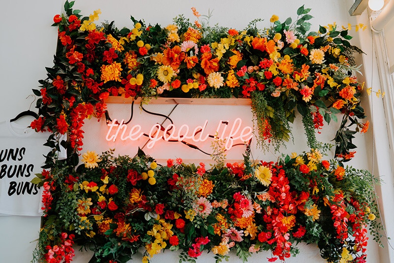A large floral arrangement encircling neon lights that read The Good Life.