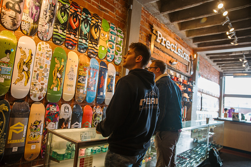 Two men survey the incredible skateboards displayed for sale on a wall.