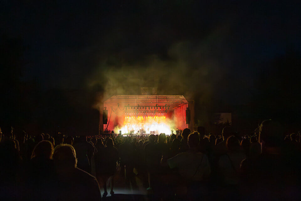 A stage glowing with bright lights as a band plays to a large crowd at night.