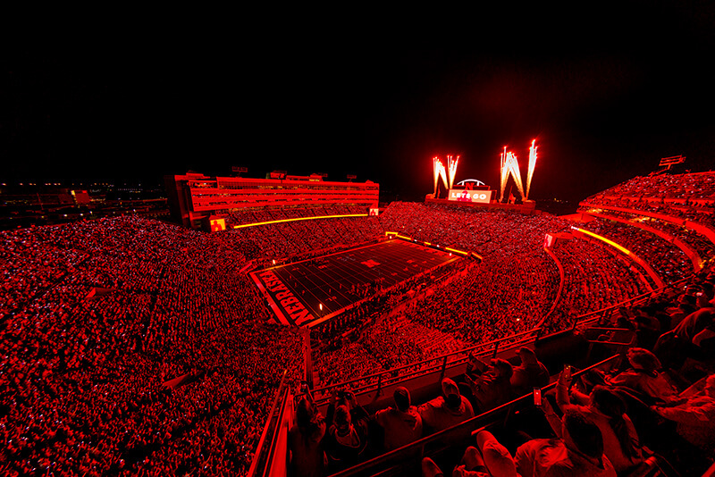 Memorial Stadium illuminated in red lights while fireworks go off during a night game.