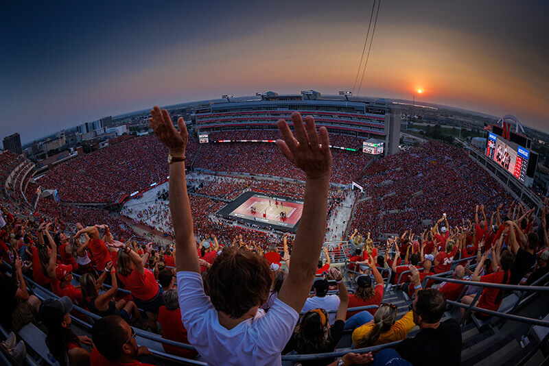 A person holds their arm up in victory from the top of the stands at Memorial Stadium during Volleyball Day.