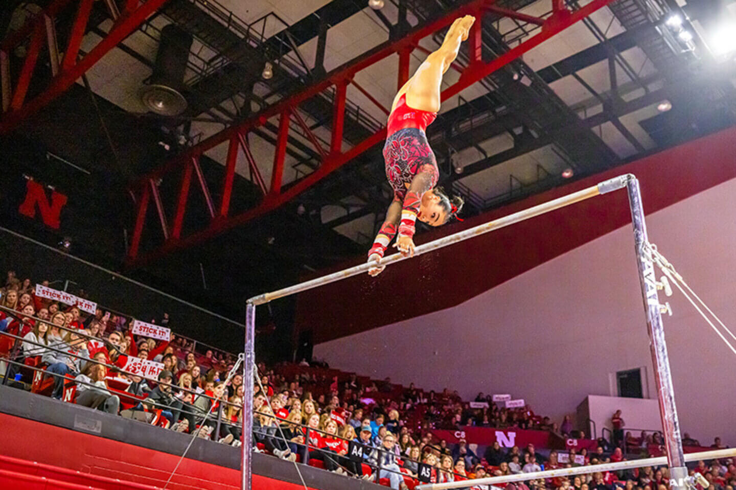 A Husker gymnast doing a handstand on a high bar.