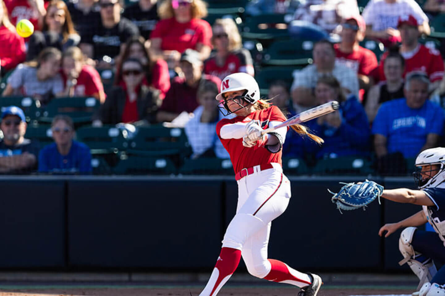 A Husker smashes a softball with a swing of her bat.